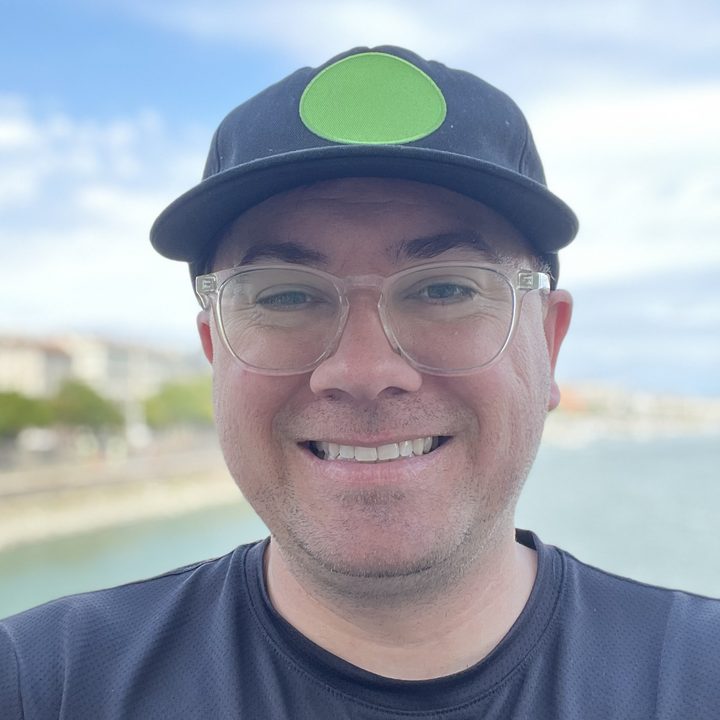 Kyle Mills, smiling, in a cap and clear glasses